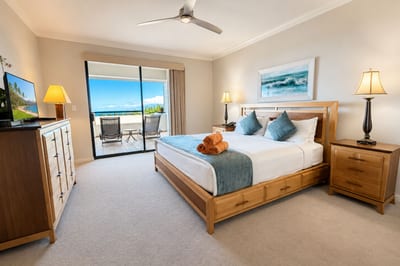 The primary bedroom's king bed opens straight onto its own private lanai, with ocean-tinged sunset views and a flat-screen TV.