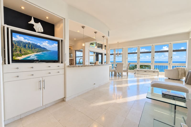 Open concept living and entertainment area with a built in flat screen TV and mirrored accent wall, with a direct sightline to the dining lanai and ocean beyond.