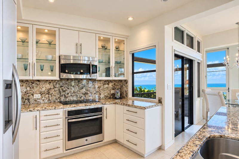 Chef's kitchen with a built in oven, glass cooktop, and mosaic tile backsplash, offering direct access to the lanai.