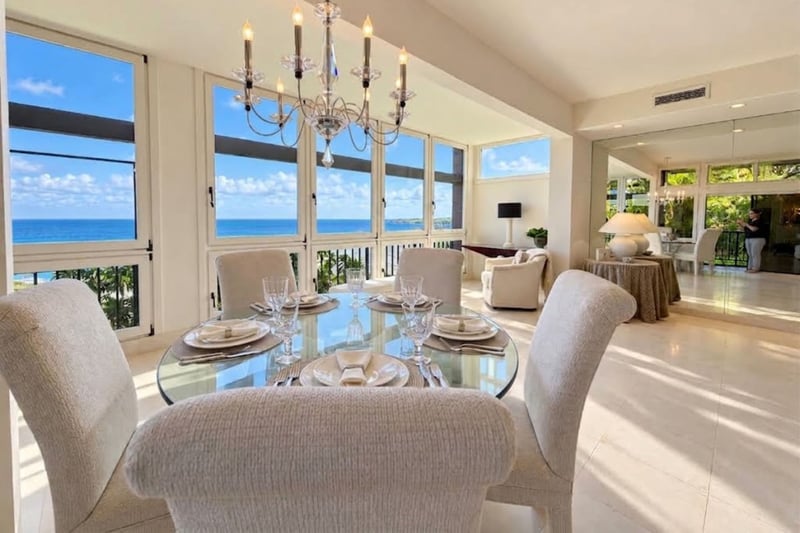Ocean view dining for six at a glass top table beneath a crystal chandelier, framed by floor to ceiling windows.