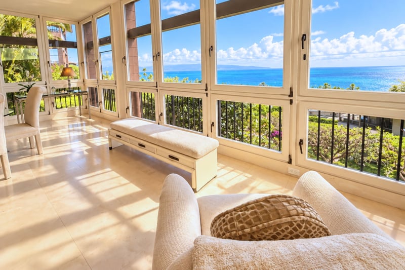 Sunlit sitting nook with a wraparound window bench framing panoramic ocean views.