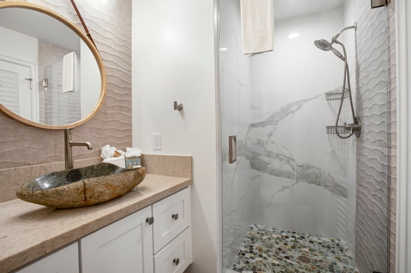 Textured wall tiles and a river rock shower floor create a calming, organic contrast to the crisp white finishes   