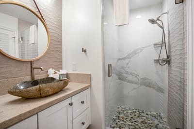 Textured wall tiles and a river rock shower floor create a calming, organic contrast to the crisp white finishes