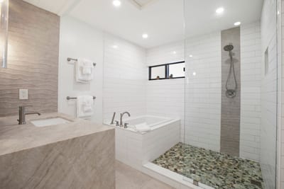 A walk-in shower with cascading pebble stone flooring and sleek vertical tile inlays sets the tone for a spa-like retreat KRV-2823