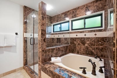 Elegant spa-style bathtub framed by rich marble and glass shower.