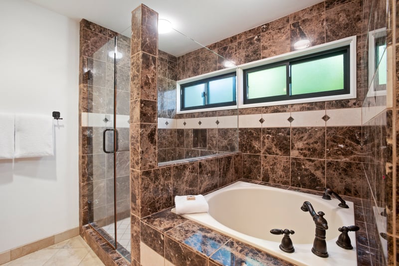 Elegant spa-style bathtub framed by rich marble and glass shower.