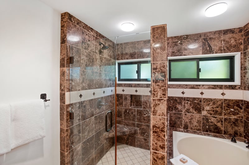 Spacious marble-tiled shower with glass enclosure and built-in bench.