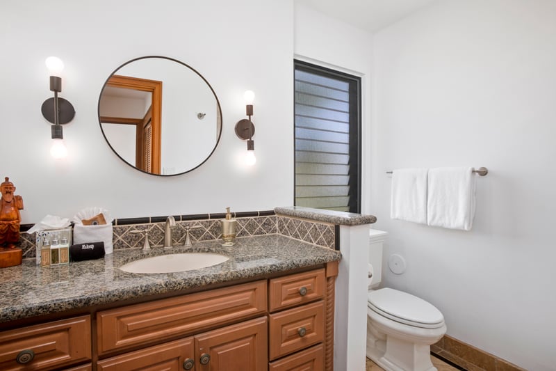 Stylish vanity with granite countertop, round mirror, and private toilet.