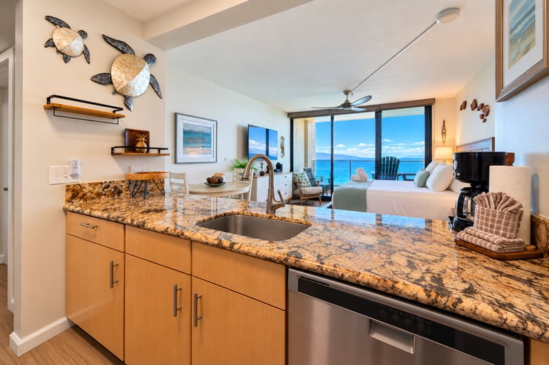 Kitchen with granite countertops, a stainless steel sink and dishwasher, and an open sightline to the ocean view living area MAH-1002