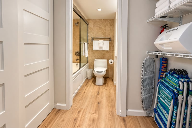 Hallway to the bathroom with a linen shelf, beach chairs, a cooler, and an ironing board in the closet MAH-1002