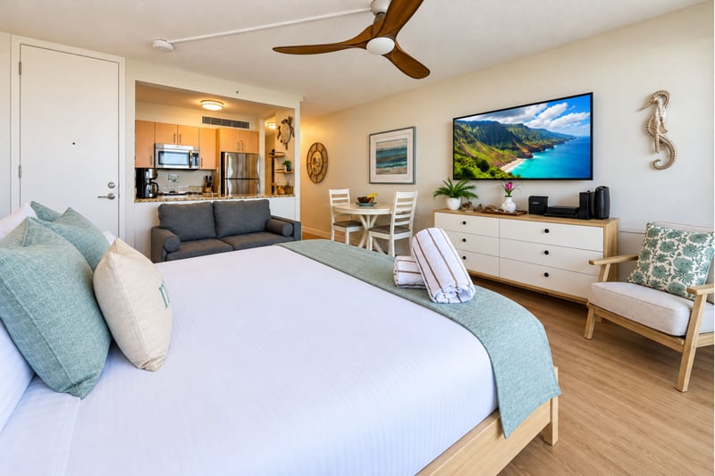 Studio with a king bed, wall-mounted TV, dresser, and a sofa beside the kitchen and dining table MAH-1002