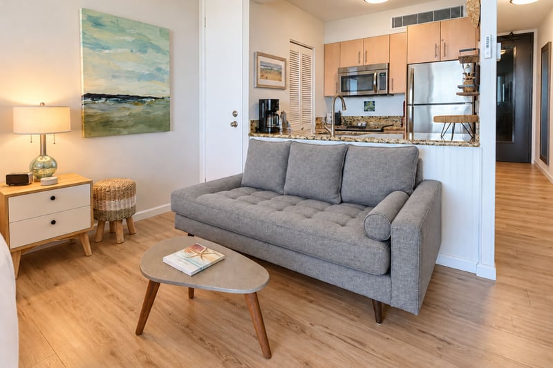 Living area with a tufted gray sofa and coffee table opening to a kitchen with stainless steel appliances and granite counters MAH-1002