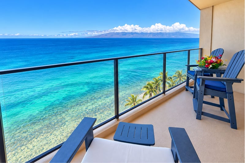 Oceanfront lanai with lounge seating and glass railings overlooking turquoise water and palm trees MAH-1002