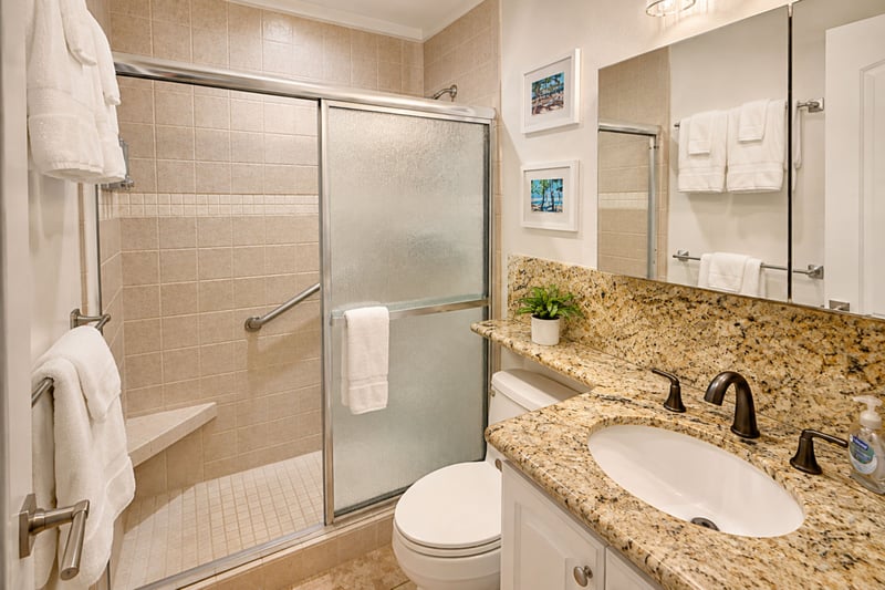 The granite-topped vanity and walk-in glass shower keep things bright and easy -- a sliding glass door, built-in shower seat and grab bar, plush white towels, and a touch of tropical wall art to set the mood.