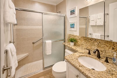 The granite-topped vanity and walk-in glass shower keep things bright and easy -- a sliding glass door, built-in shower seat and grab bar, plush white towels, and a touch of tropical wall art to set the mood.