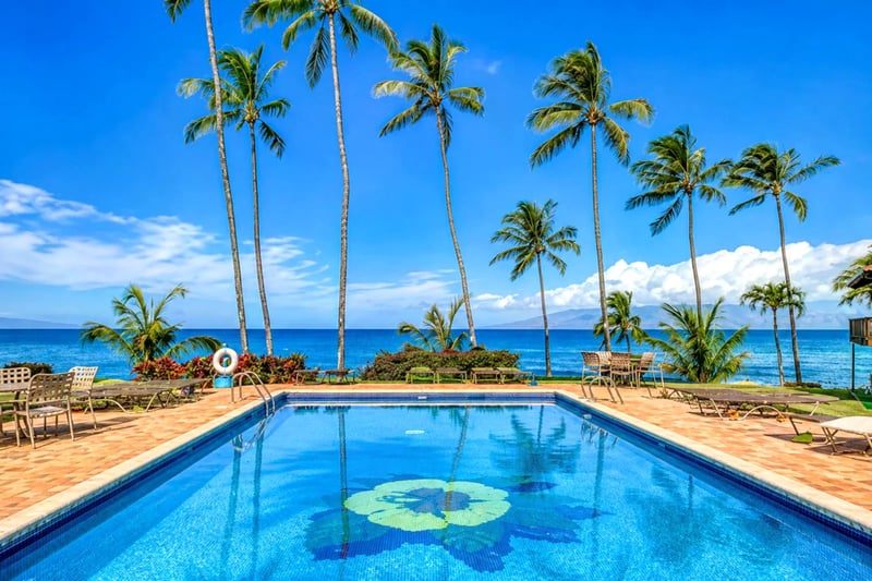 Oceanfront pool at Mahina Surf — hibiscus-tiled pool framed by swaying palms with views toward Lanai and Molokai
