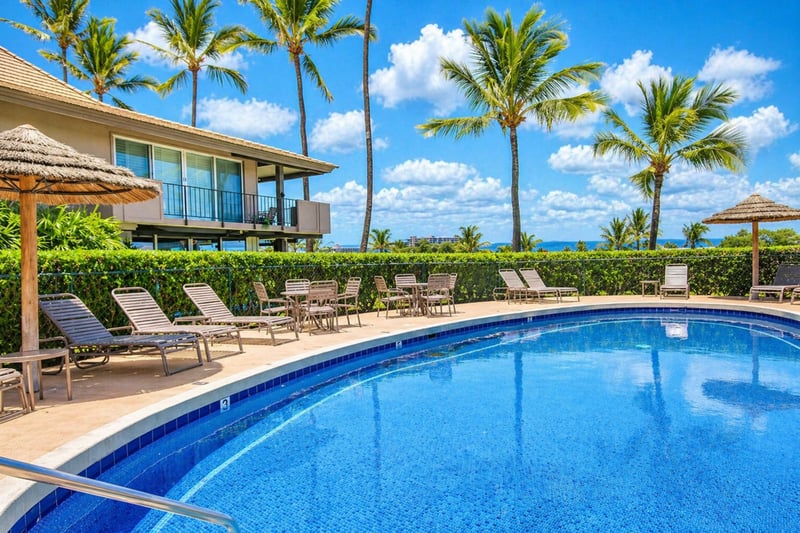 Resort pool at Maui Eldorado H207 — palm-lined deck with loungers, shaded cabanas, and ocean views