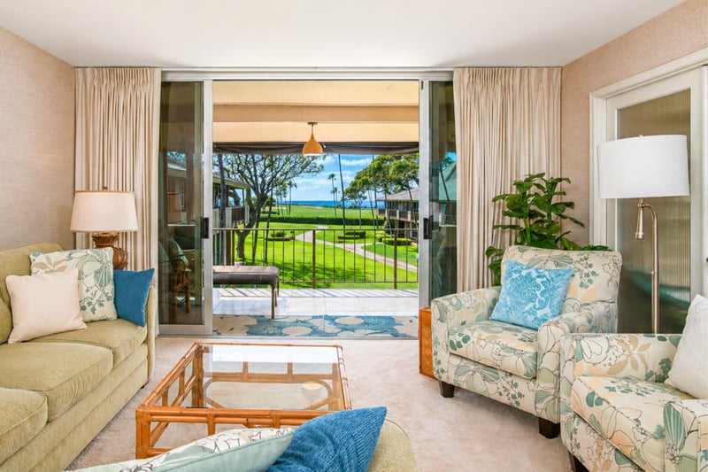 Living room seating at Maui Eldorado H207 — floral armchairs beside sliding doors to the covered lanai and golf-course lawn