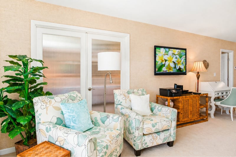 Second living area at Maui Eldorado H207 — matching floral armchairs, wall-mounted TV, and French doors to the primary suite