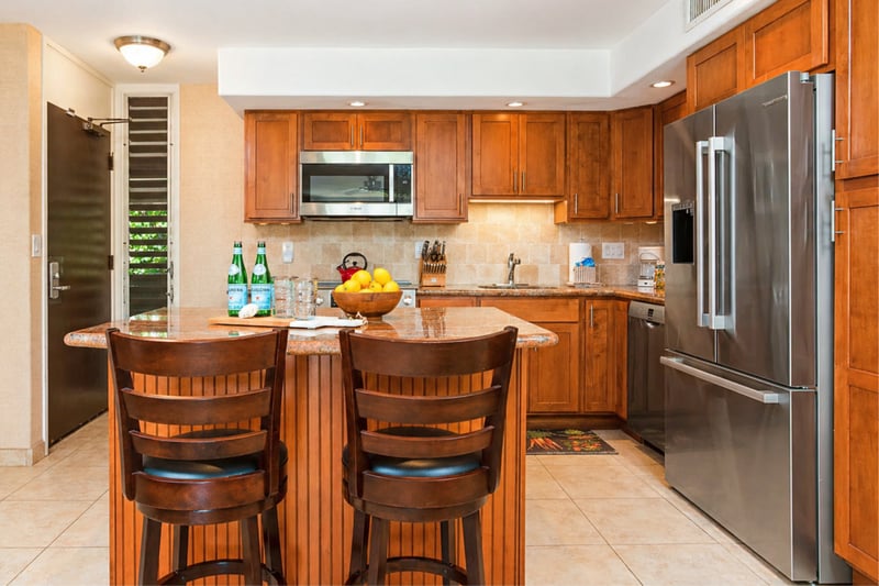 Kitchen island seating at Maui Eldorado H207 — granite bar with two barstools, stainless refrigerator, and full-size dishwasher