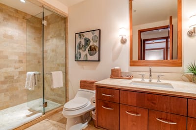 A walk-in glass shower framed in stone invites guests to refresh in understated luxury and warm natural textures