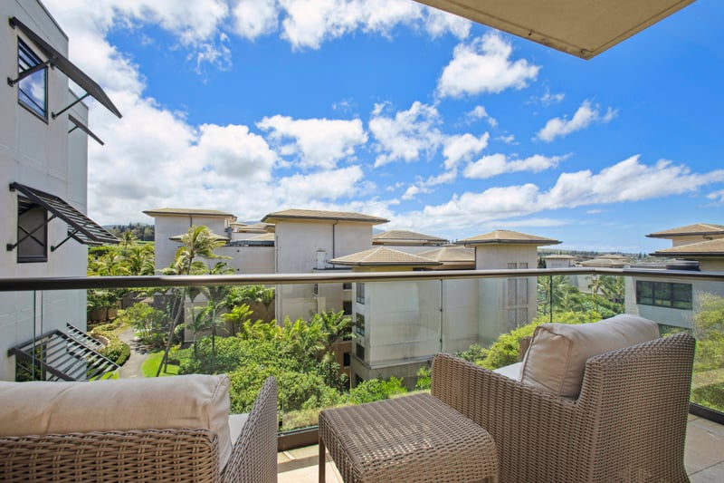 The room flows seamlessly toward a private lanai, where swaying palms and ocean blues stretch to the horizon   
