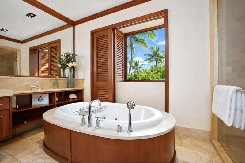 A large soaking tub sits beneath bright lighting and rich wood trim, offering a peaceful end to beach days. MON-2204
