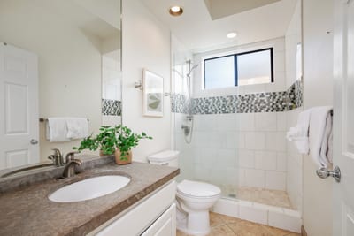 A crisp and modern guest bath featuring a stone vanity, glass walk-in shower, and mosaic tile accents for fresh appeal