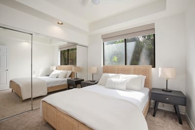 Refined simplicity meets comfort—this guest room glows with soft light, mirrored charm, and crisp linens