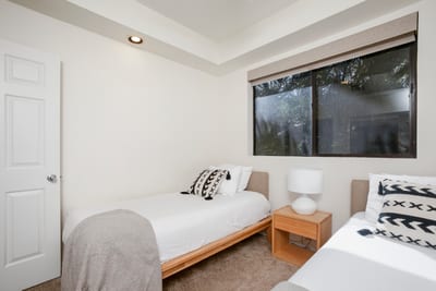 A simple sanctuary with twin beds, cozy throws, and sunlight filtering through peaceful green views