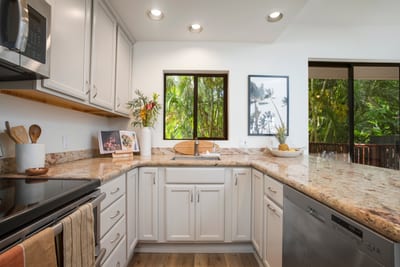 This airy, modern kitchen features granite counters, sleek appliances, and views of lush tropical greenery outside