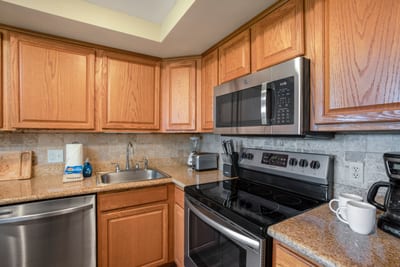A cheerful kitchen with stainless steel appliances, soft lighting, and comfy stools perfect for casual dining NAP-A25