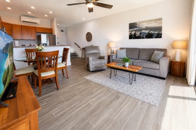 Living and dining area at Napili Point B31 — plush recliner, sofa seating, and a four-top dining table under swaying ceiling fans