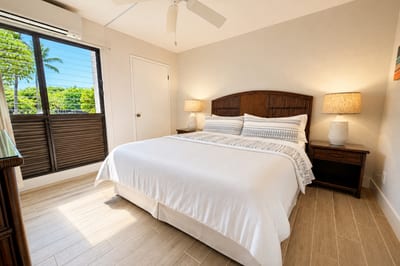 Primary bedroom at Napili Point B31 — king bed, private lanai access, and lush tropical views through the sliding glass door