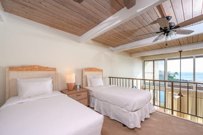 Twin guest loft with vaulted wood ceilings, tropical accents, large windows, and views of blue skies and palms NAP-C18
