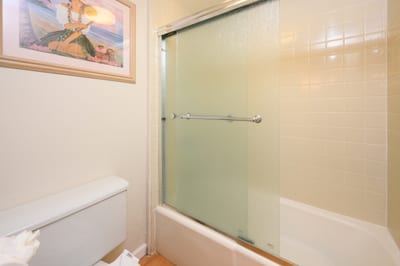 Encased in frosted glass, the shower-tub combo offers privacy and comfort, surrounded by clean, glossy cream-toned tiles