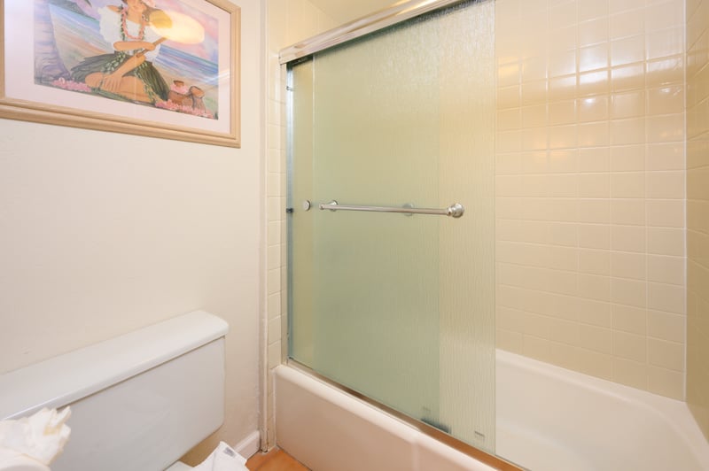 Encased in frosted glass, the shower-tub combo offers privacy and comfort, surrounded by clean, glossy cream-toned tiles
