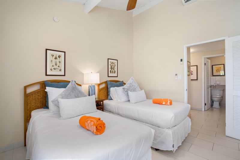 Twin-bed guest room with vaulted ceilings, bright windows, tropical accents, and warm wood furniture for pure comfort