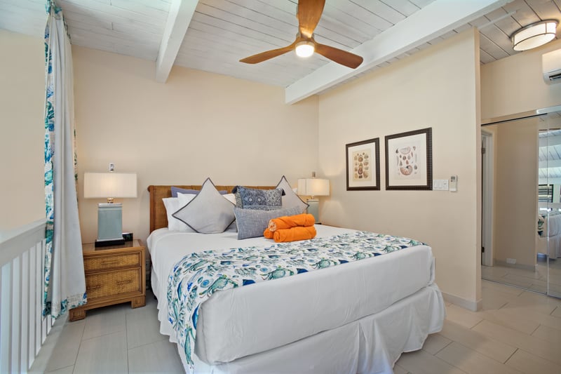 Spacious master suite with blue botanical accents, vaulted ceilings, wood furnishings, and sunlit balcony charm