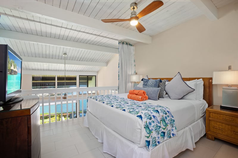 Elegant master with tropical flair, vaulted white ceilings, pool views, cozy textures, and smart TV comforts.