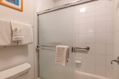 Enclosed in frosted glass and lined with glossy white tile, this inviting shower offers a refreshing escape in clean simplicity