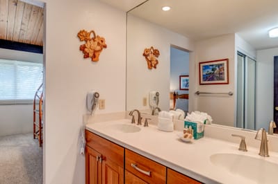 The spacious dual-sink vanity offers generous counter space, framed by a wide mirror and soft natural light from twin windows. NAP-C42