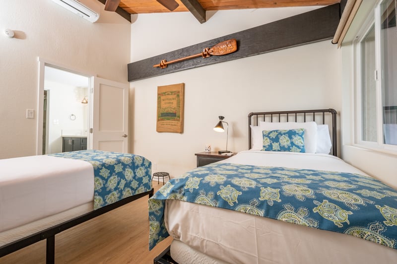 Stylish guest room with twin beds, vaulted ceilings, tropical prints, and bright views of lush garden greenery NAP-C43
