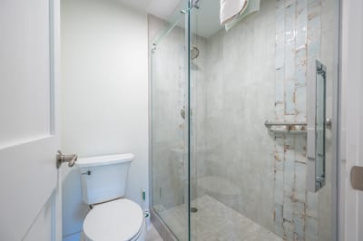 The frameless glass shower reveals a striking blend of stone tiles with vertical accents, adding depth and quiet drama