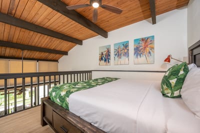 Lofted master suite with wood beam ceilings, tropical leaf bedding, palm wall art, and warm modern accents