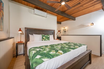 Elegant loft-style master with king bed, island artwork, exposed beams, and soft light from balcony rail views