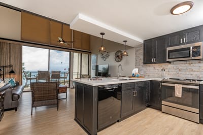 This striking kitchen features dark cabinetry, quartz-style counters, vaulted ceilings, and stunning ocean views