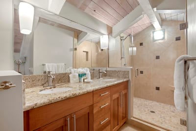 Vaulted ceilings and wood beams crown this elegant master bath, where granite counters meet a spacious walk-in shower