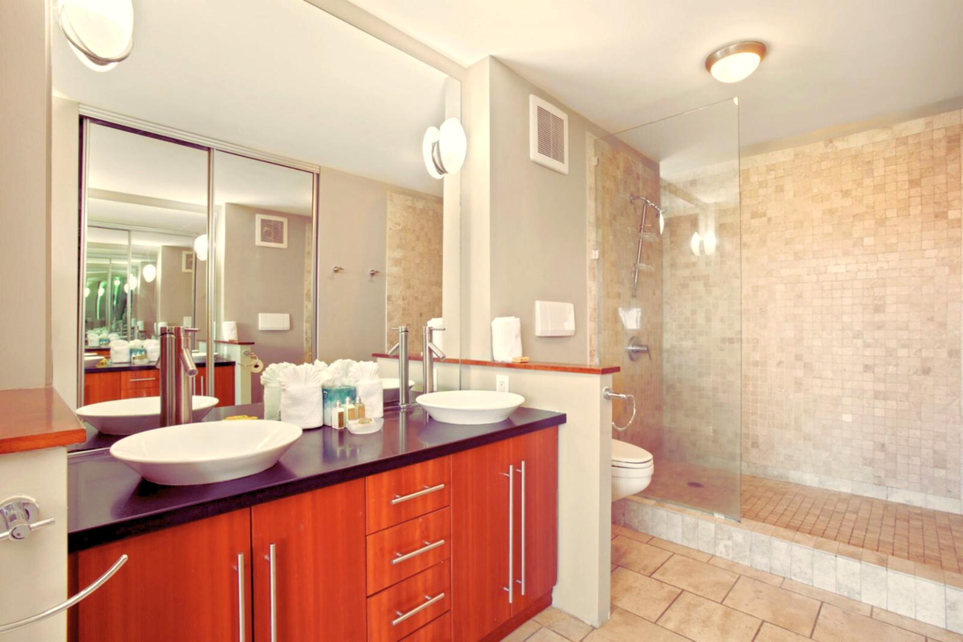 This stunning master bath showcases dual vessel sinks, custom cabinetry, and a spacious walk-in shower wrapped in stone