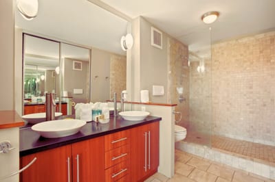 This stunning master bath showcases dual vessel sinks, custom cabinetry, and a spacious walk-in shower wrapped in stone